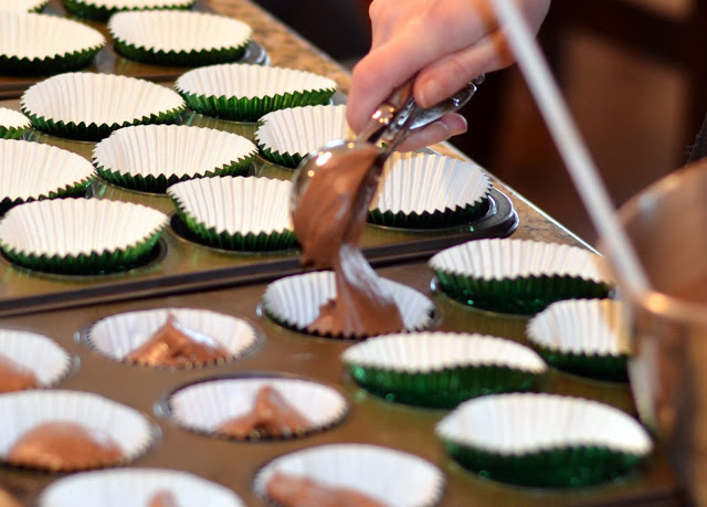 using a scoop to put cupcake batter into cupcake pans filling cupcake tins